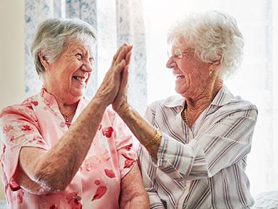 two elderly women high-fiving at The Delaney at Georgetown senior living community