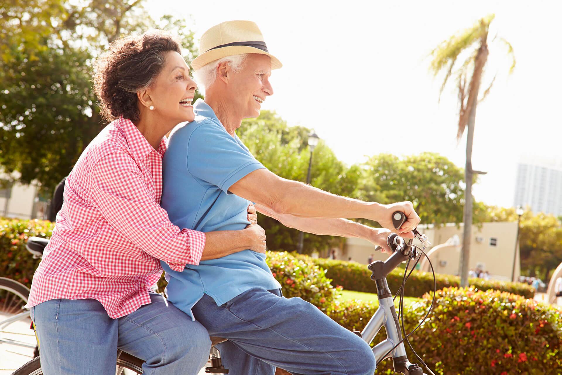 elderly couple enjoying independent living together riding a bike at The Delaney at Georgetown