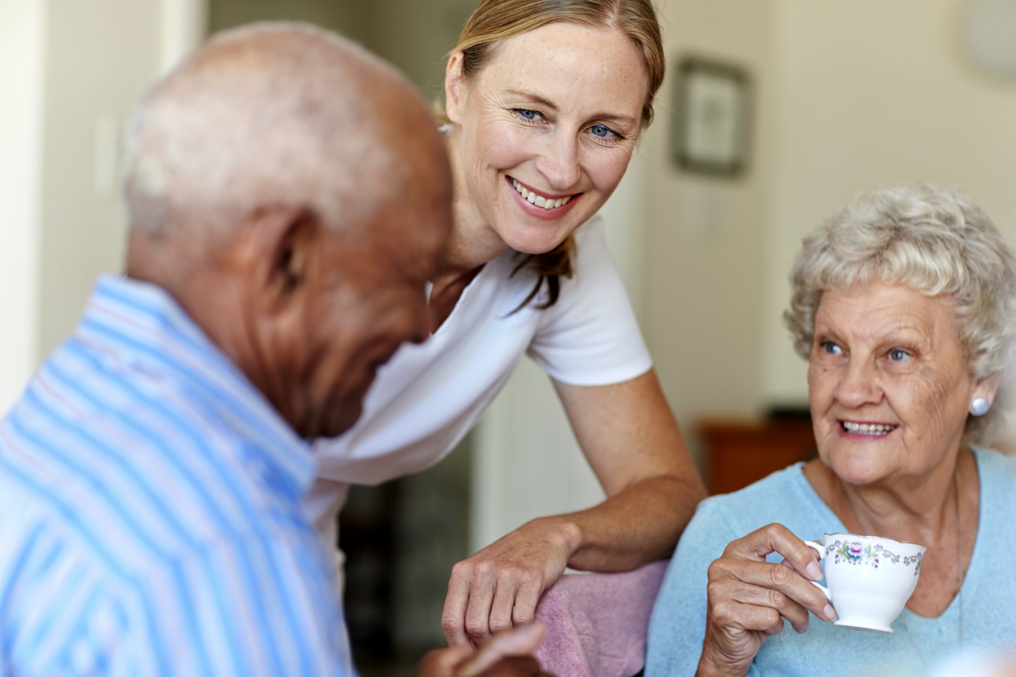 Smiling caregiver with two elderly residents sharing a joyful moment with tea.