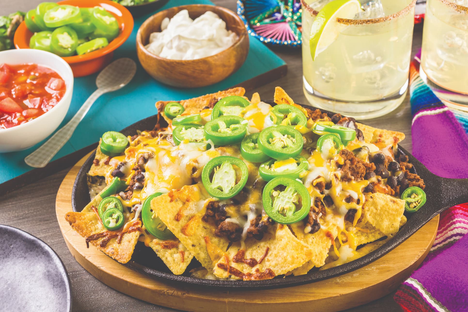 Plate of nachos with margarita and salsas near by