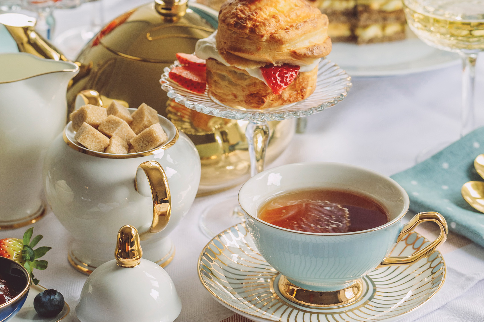 cup of tea surrounded by pastries and container of sugar cubes